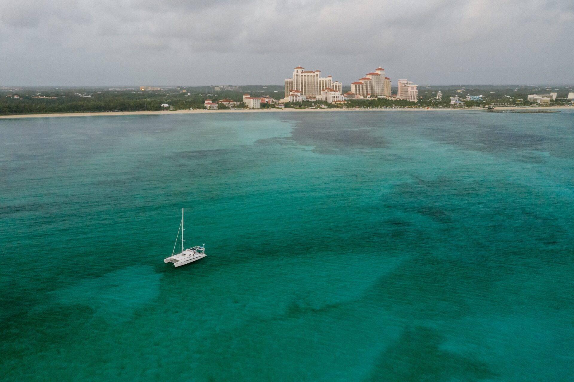 Un voilier blanc mouillé en eaux turquoise cristallines face à des hôtels resort sur une côte tropicale