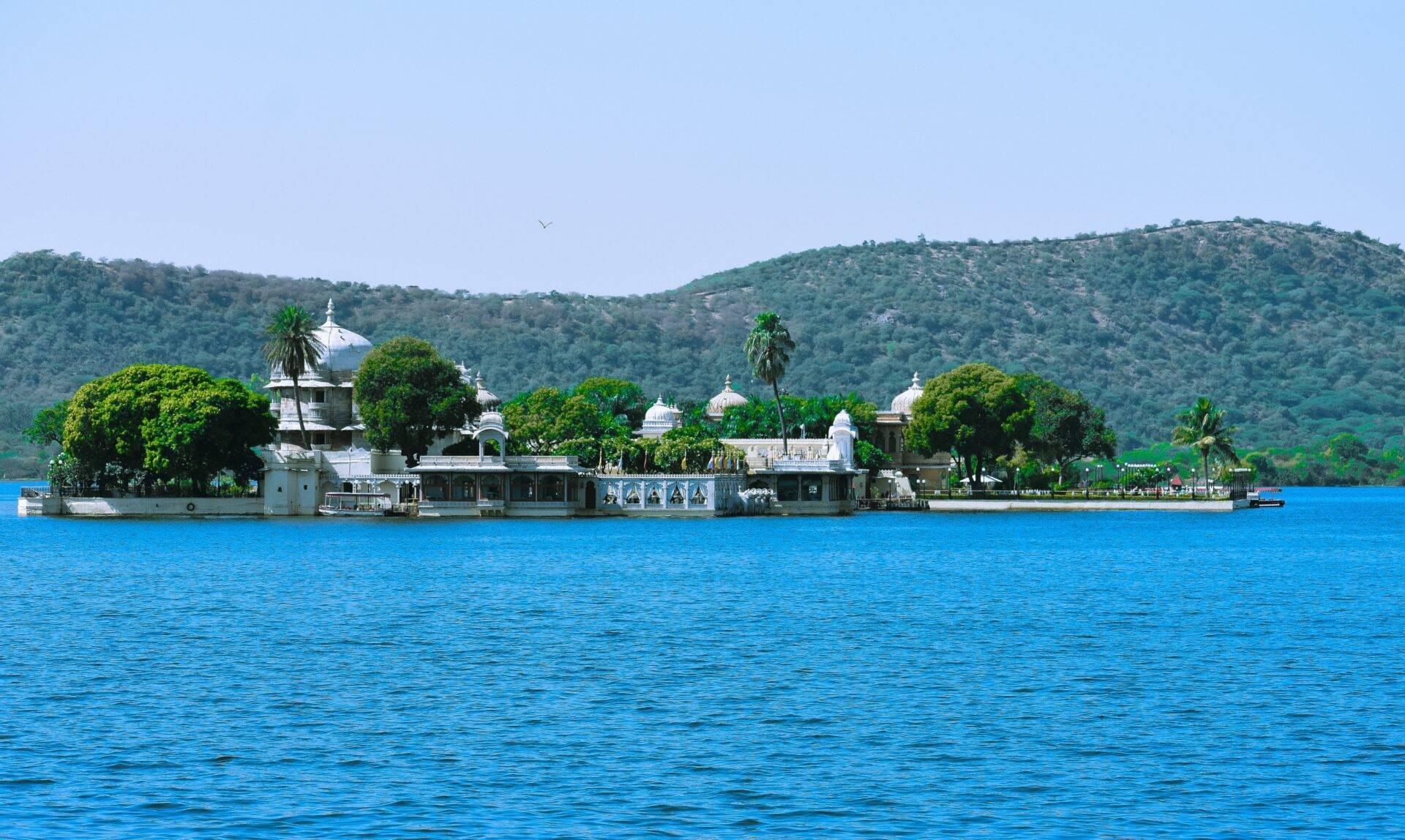 White domed temple on the banks of a blue lake, surrounded by greenery and wooded hills