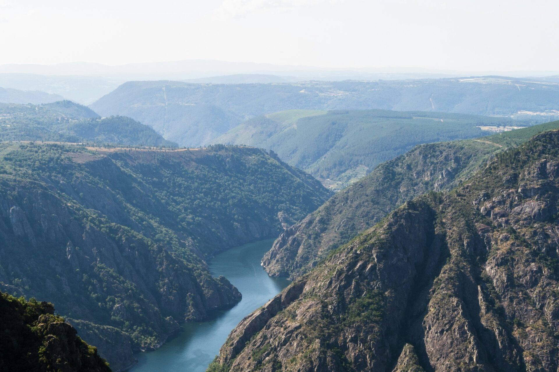 Gorge profonde avec rivière turquoise sinueuse entourée de falaises rocheuses boisées et de montagnes lointaines