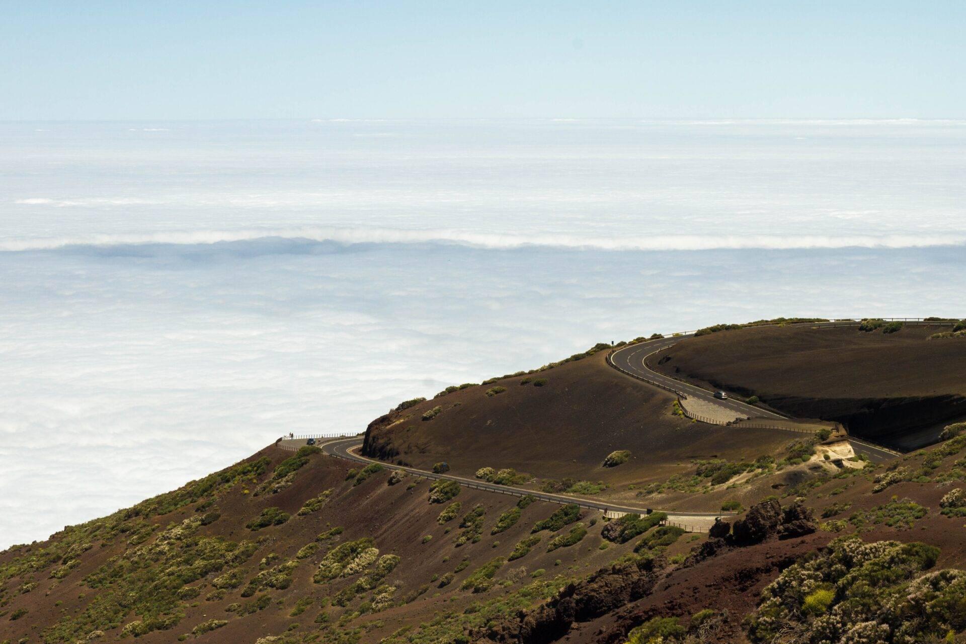 Route sinueuse traversant un cratère volcanique aride avec vue sur la mer et les nuages en arrière-plan