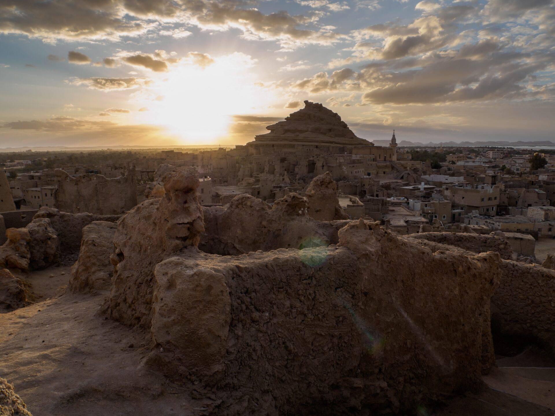 Panoramic view of an ancient stone citadel at sunset, rising above a desert settlement in Egypt