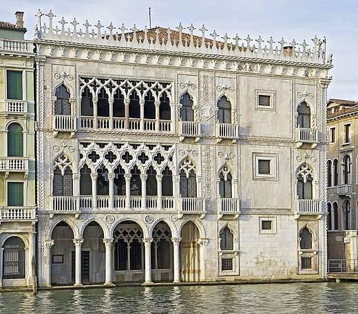 Venetian Gothic facade in white and pink marble with pointed arched arcades reflected in the canal water