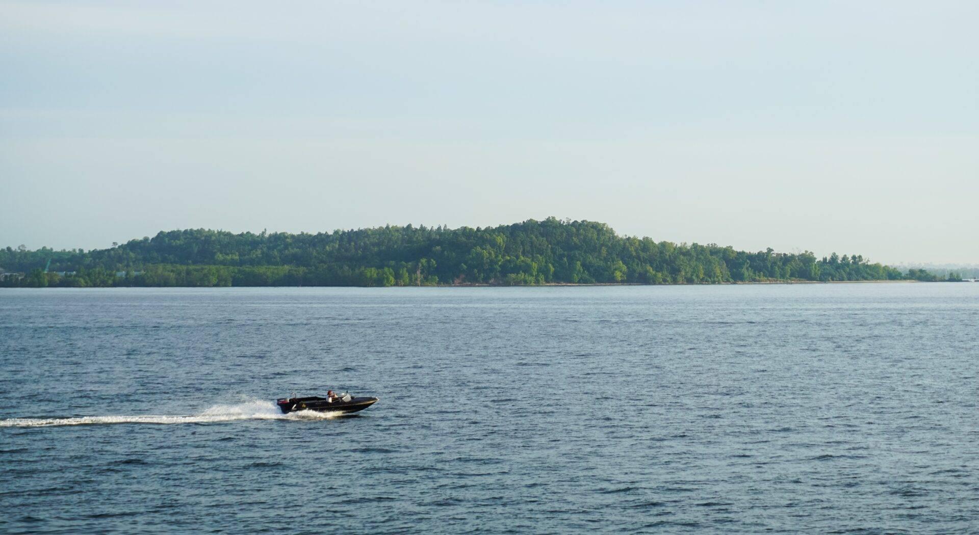 A motorboat travels across a calm lake bordered by dense, verdant forest