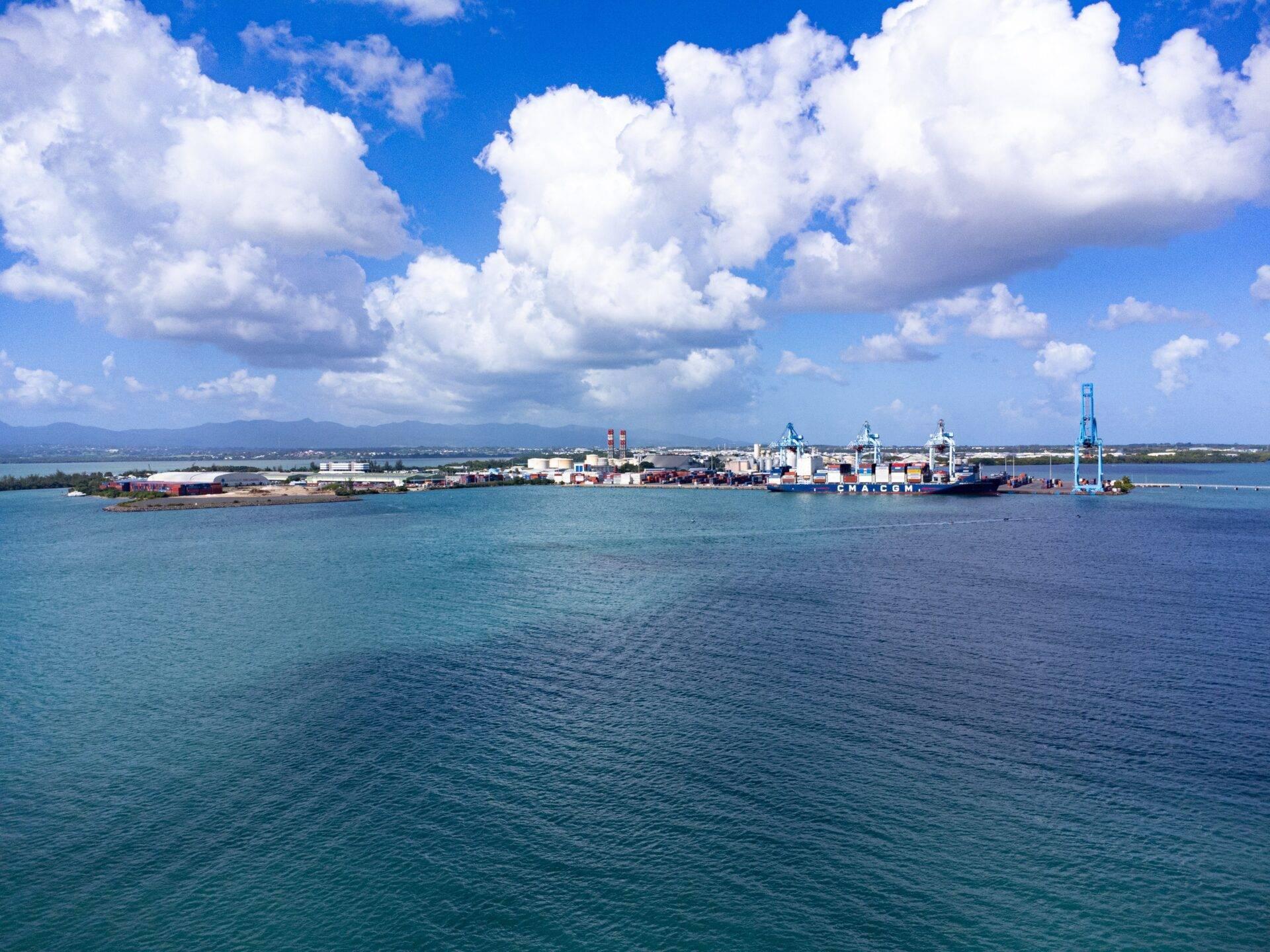Vue panoramique d’un port maritime tropical avec navire de cargo, installations portuaires et montagnes en arrière-plan