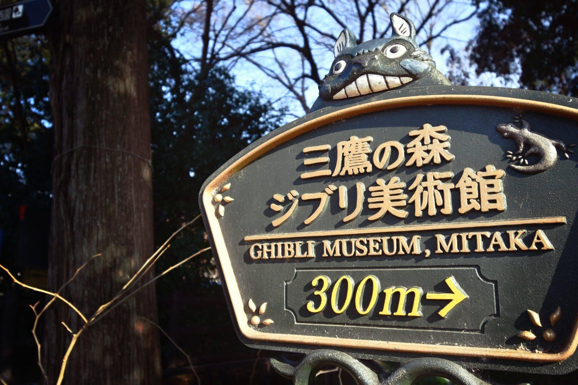Signpost to the Ghibli Museum Mitaka decorated with a fantastical creature, set within a Japanese forest