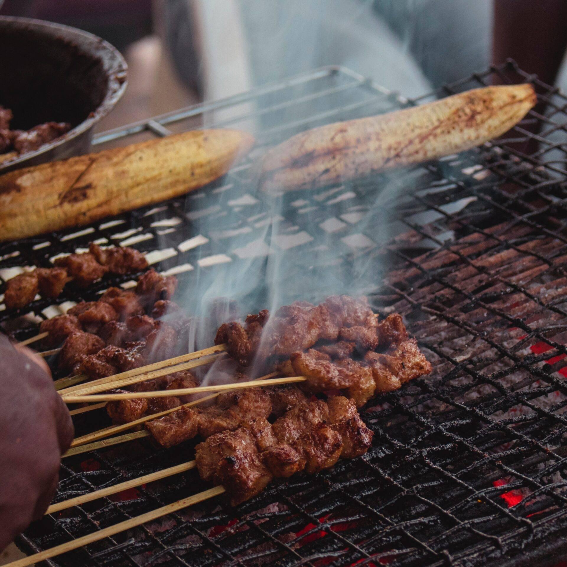 Brochettes de viande grillées sur un barbecue fumant avec bananes plantains, cuisine camerounaise traditionnelle