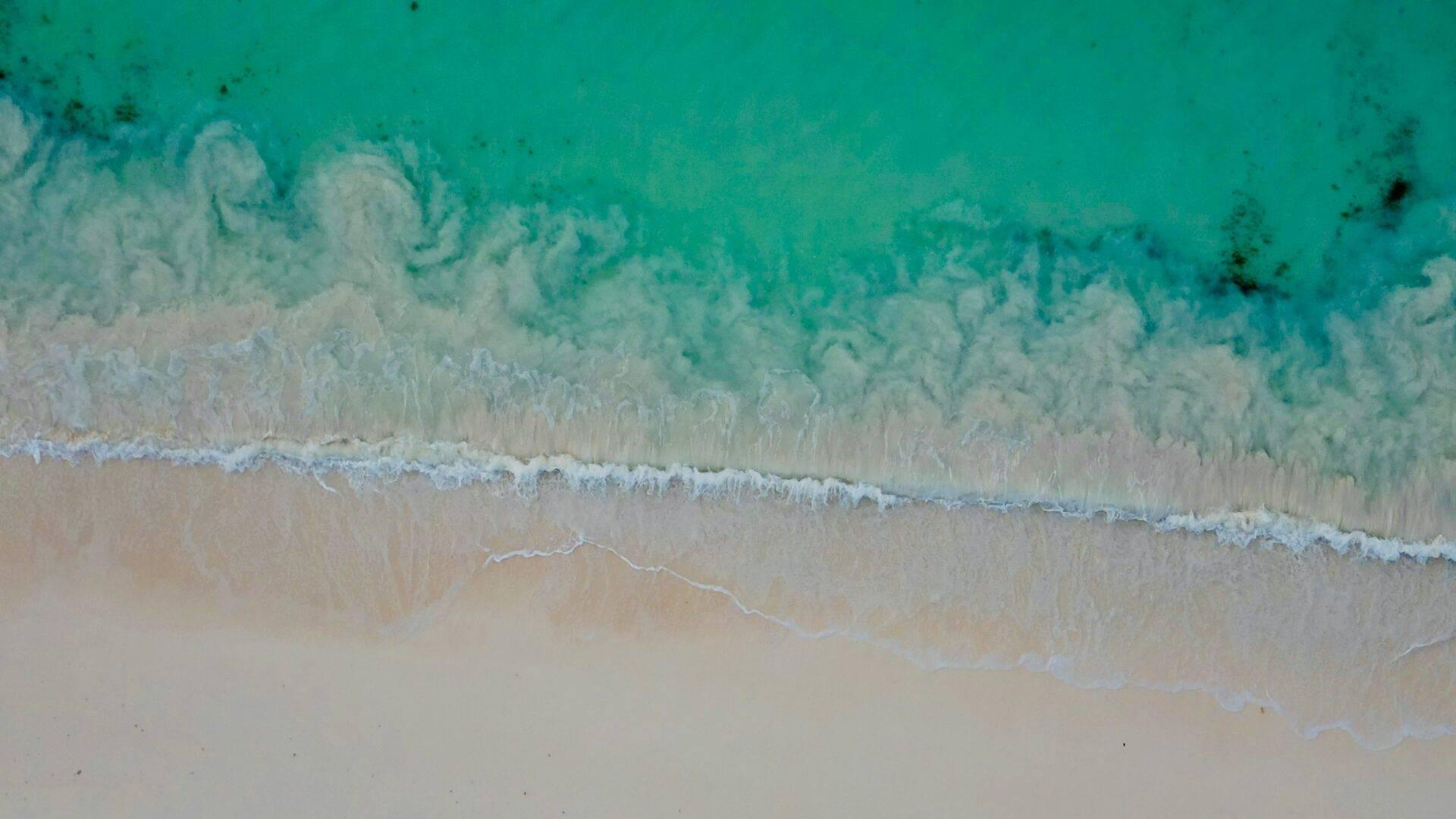 Vue aérienne d’une plage de sable blanc avec des vagues turquoise et cristallines s’échouant sur le rivage