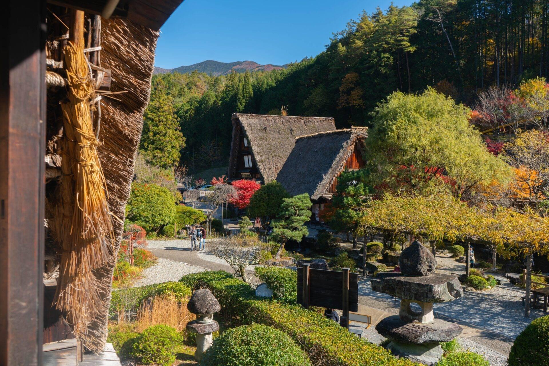Traditional Japanese village with thatched-roof houses, landscaped gardens and wooded mountains in the background