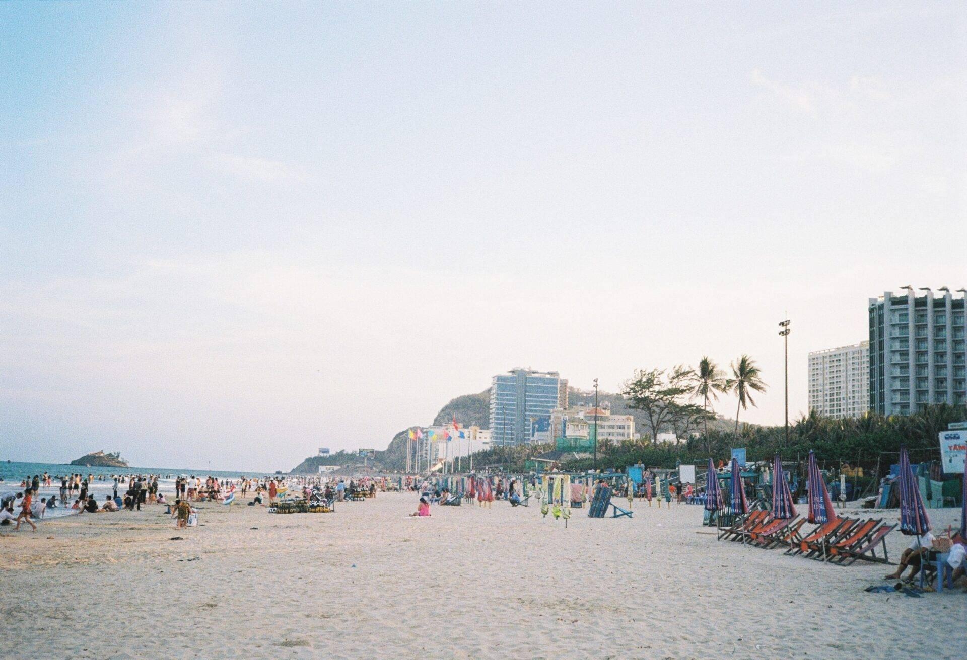 Une plage de sable blanc bondée avec des chaises longues colorées, des immeubles modernes et des palmiers en arrière-plan