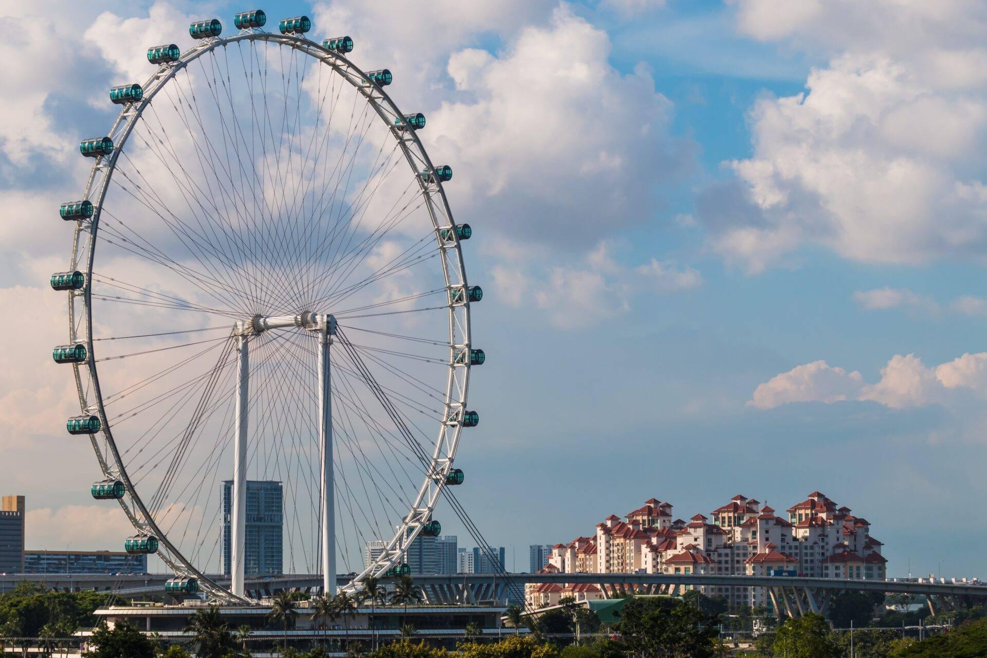 Une grande roue d’observation blanche avec cabines vertes surplombe des gratte-ciel et bâtiments résidentiels sous un ciel bleu nuageux