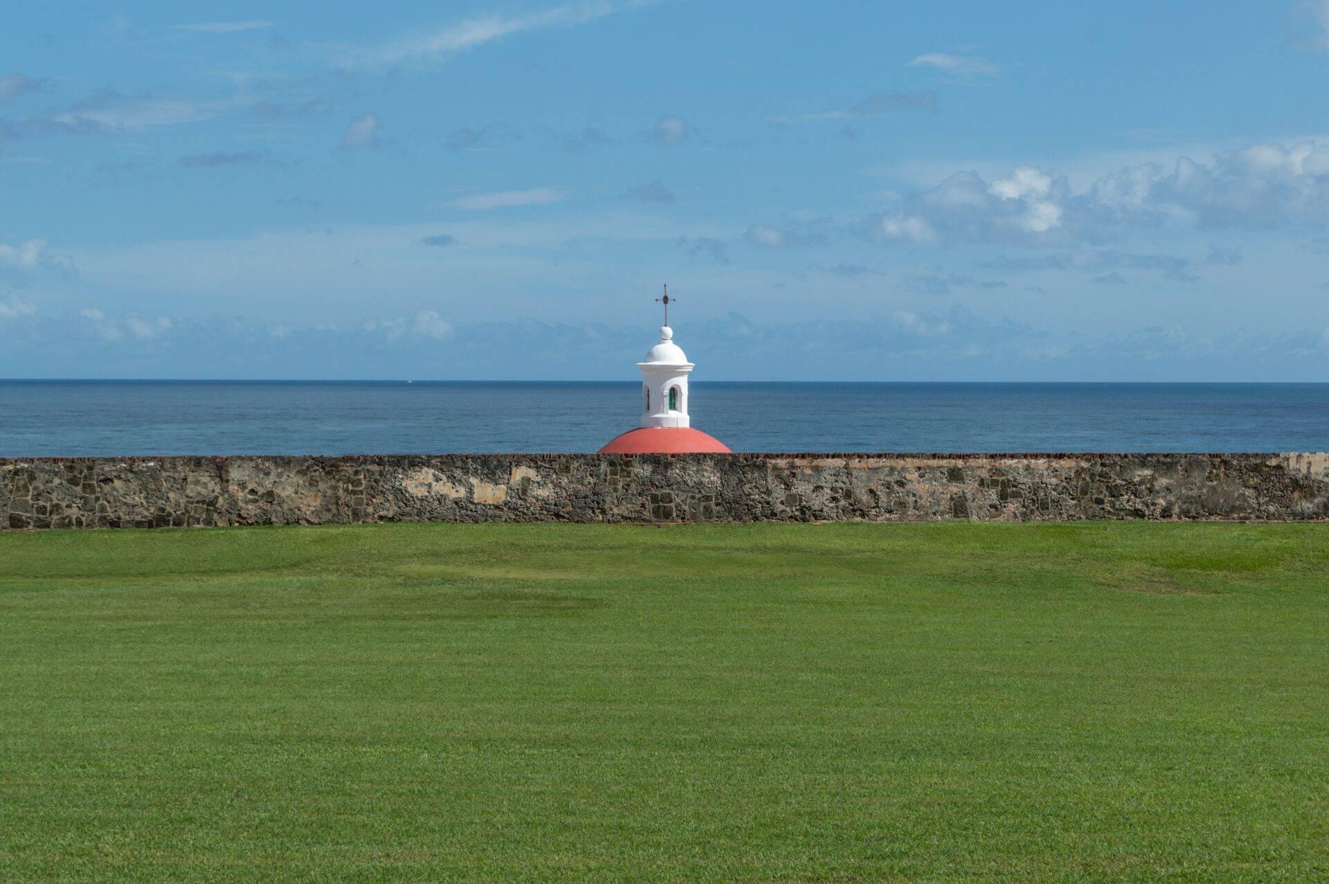 Une petite chapelle blanche au dôme rouge surplombe une forteresse en pierre face à l’océan turquoise