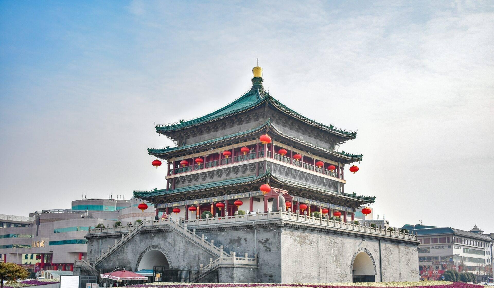 Une tour traditionnelle chinoise à étages avec toits verts recourbés, lanternes rouges et base en pierre blanche