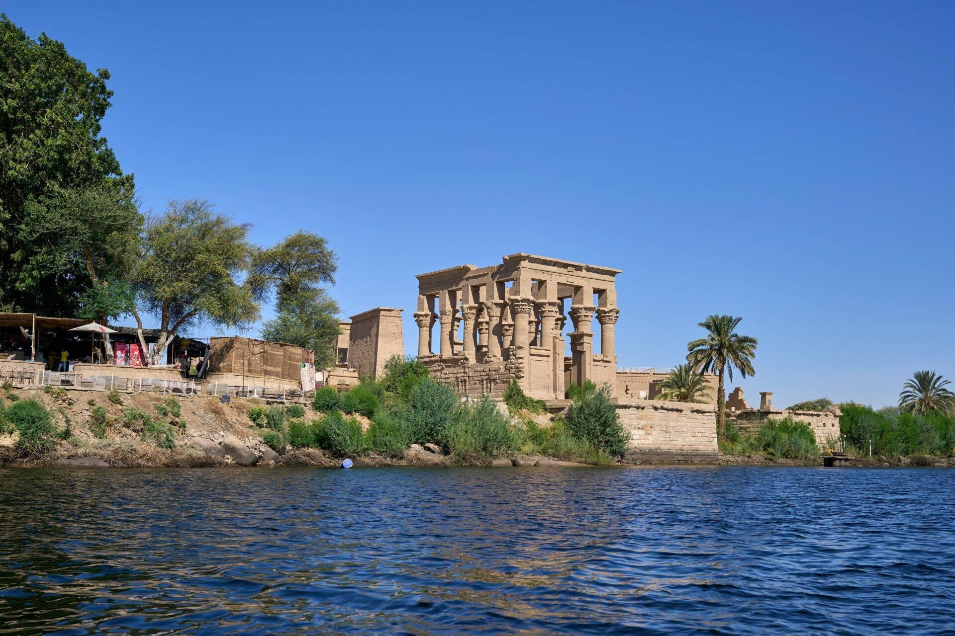Ruins of an ancient temple on the banks of the Nile with imposing columns and palm trees under a clear blue sky