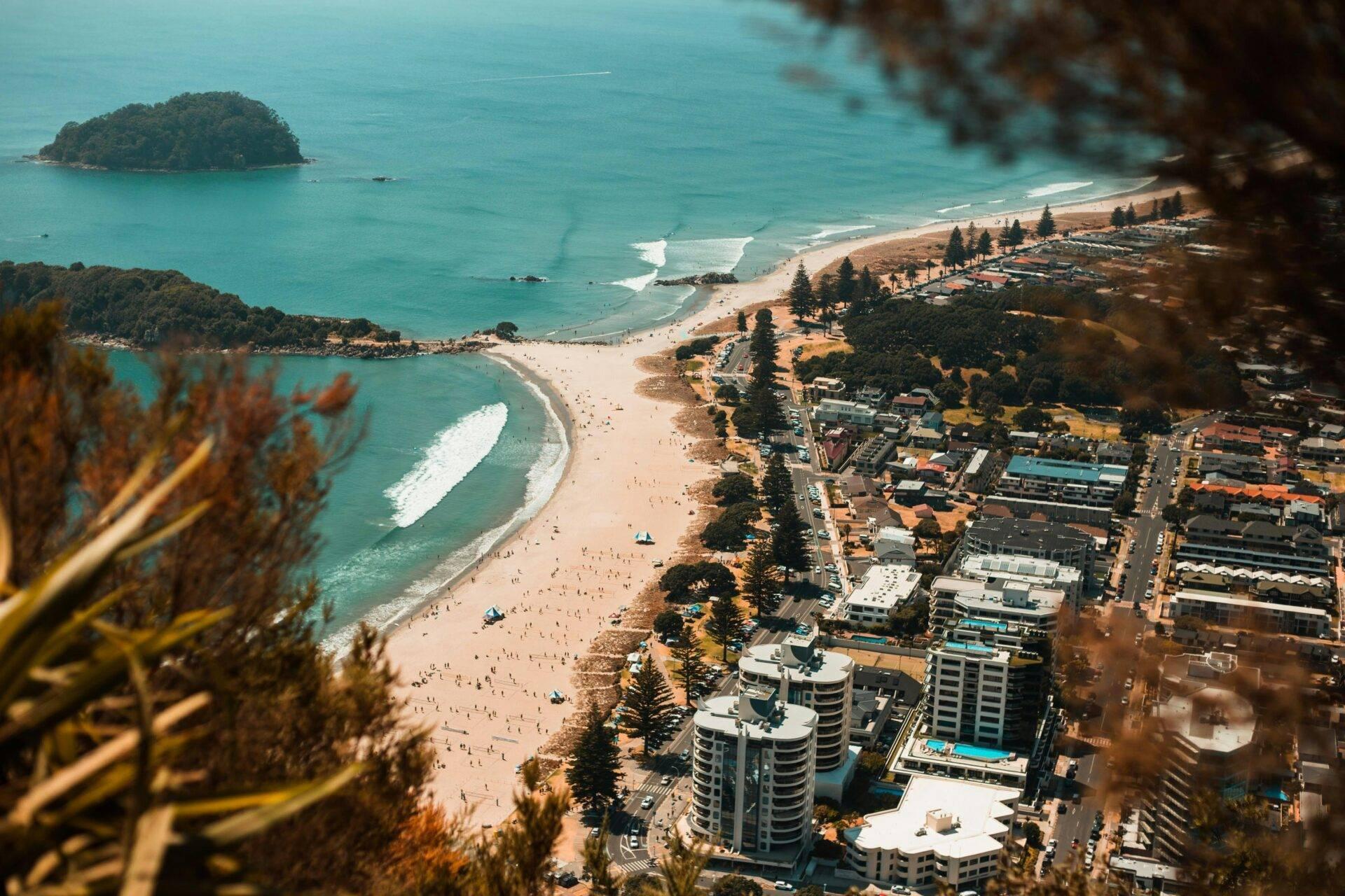 Vue aérienne d’une plage urbaine avec gratte-ciel, îlot boisé et eaux turquoise cristallines