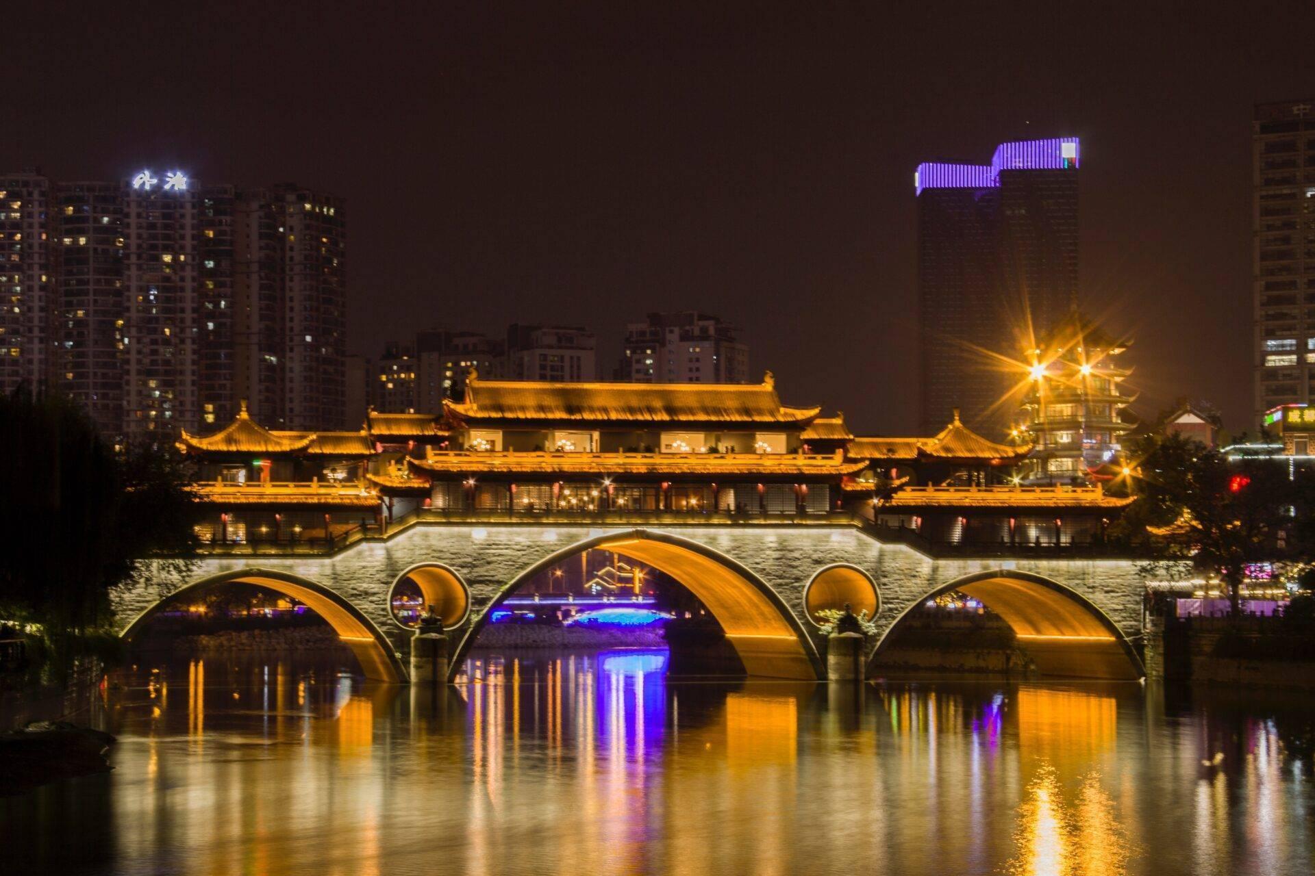 Un temple traditionnel asiatique illuminé la nuit avec un pont en pierre arqué enjambant une rivière