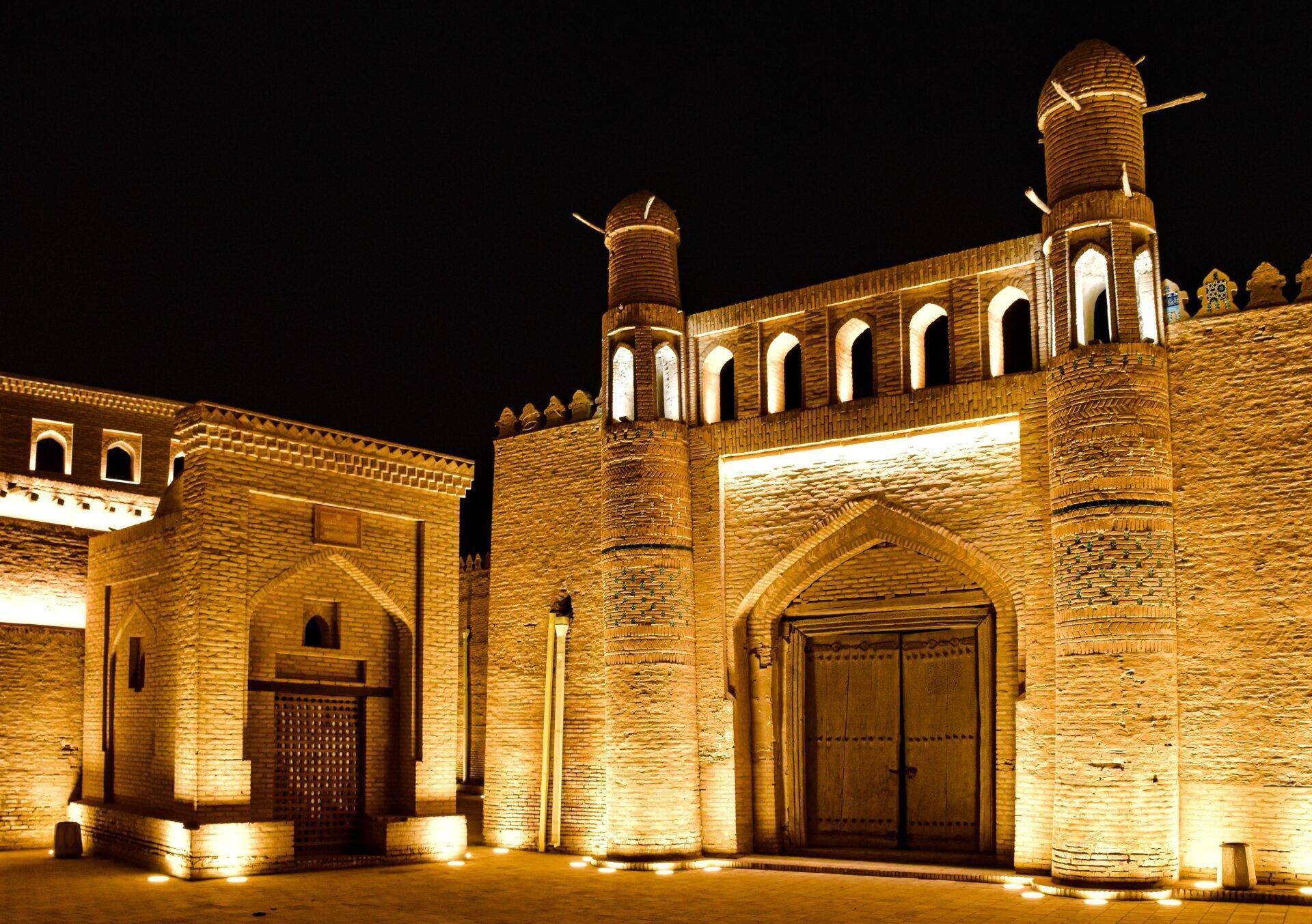 Historic brick mosque lit up at night with minarets and the characteristic arcaded architecture of Central Asia