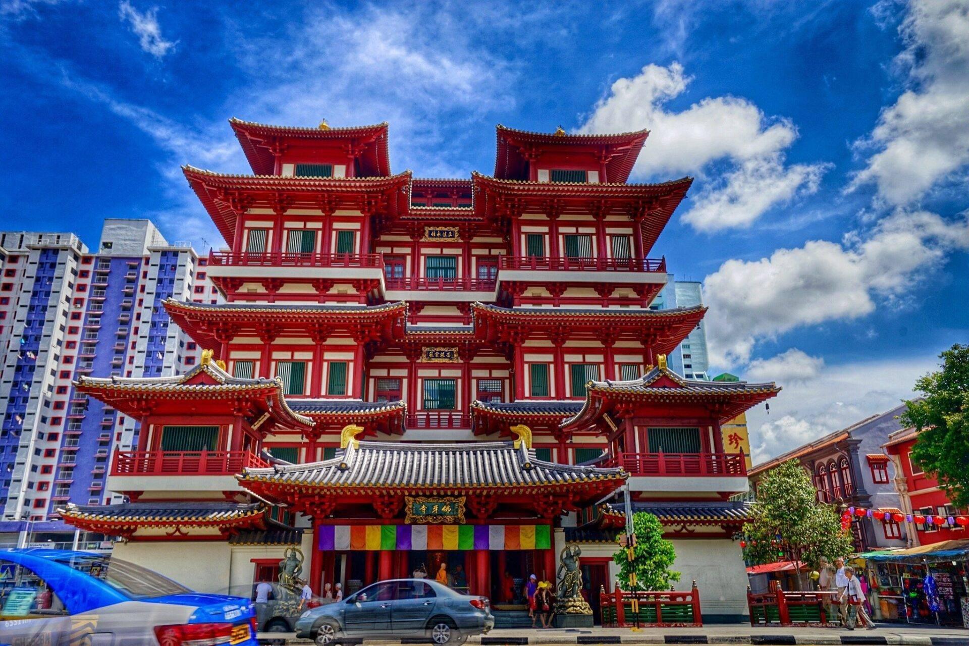 Un temple bouddhiste rouge aux toits pointus caractéristiques, entouré de bâtiments modernes sous un ciel bleu dégagé
