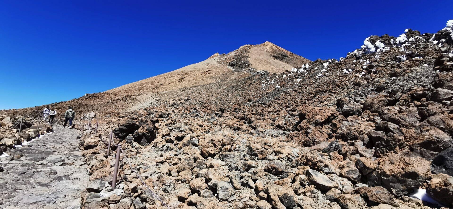 Randonneurs gravissant un sentier rocailleux vers un sommet aride sous un ciel bleu dégagé