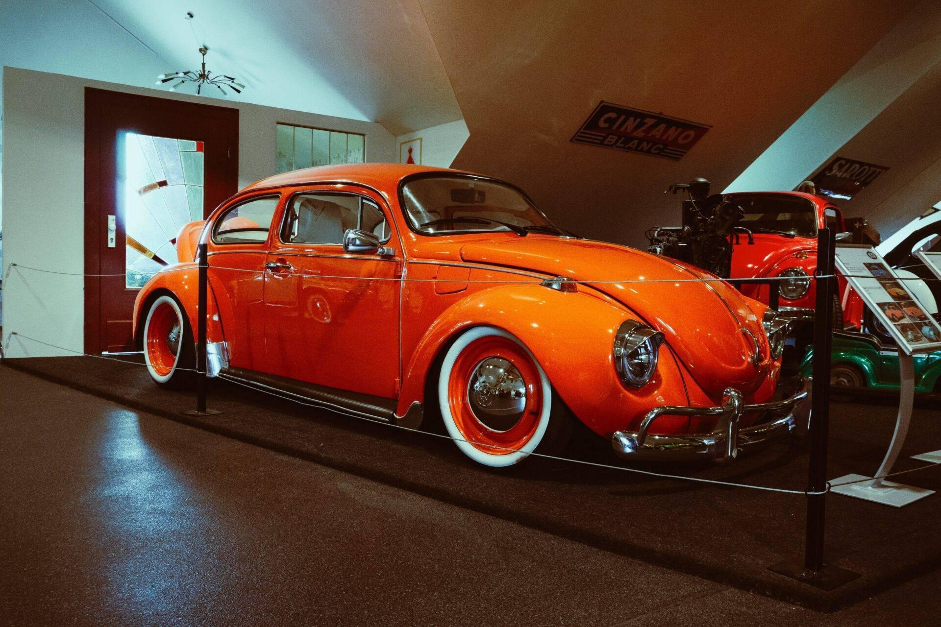 A restored red Volkswagen Beetle on display inside a covered automobile museum
