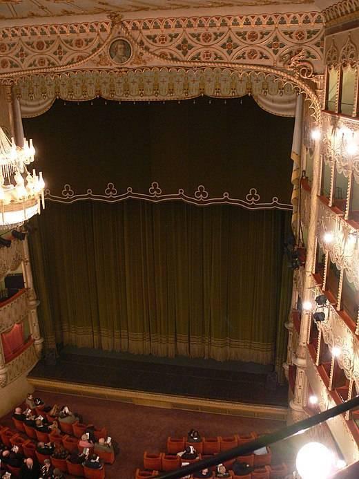 Ornate interior of a historic theatre with a dark green curtain and illuminated balconies