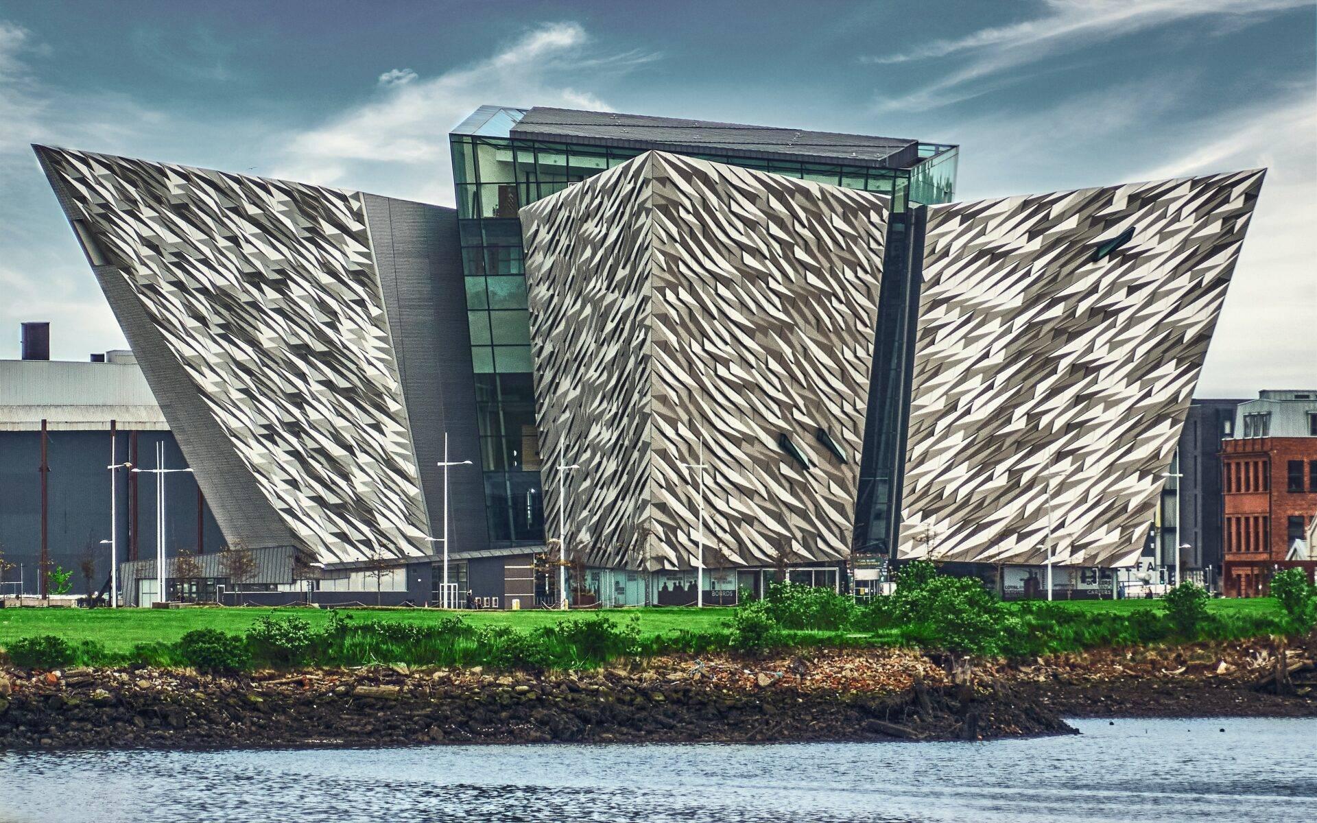 A modern building with geometric white inclined facades situated on the waterfront with a green landscape