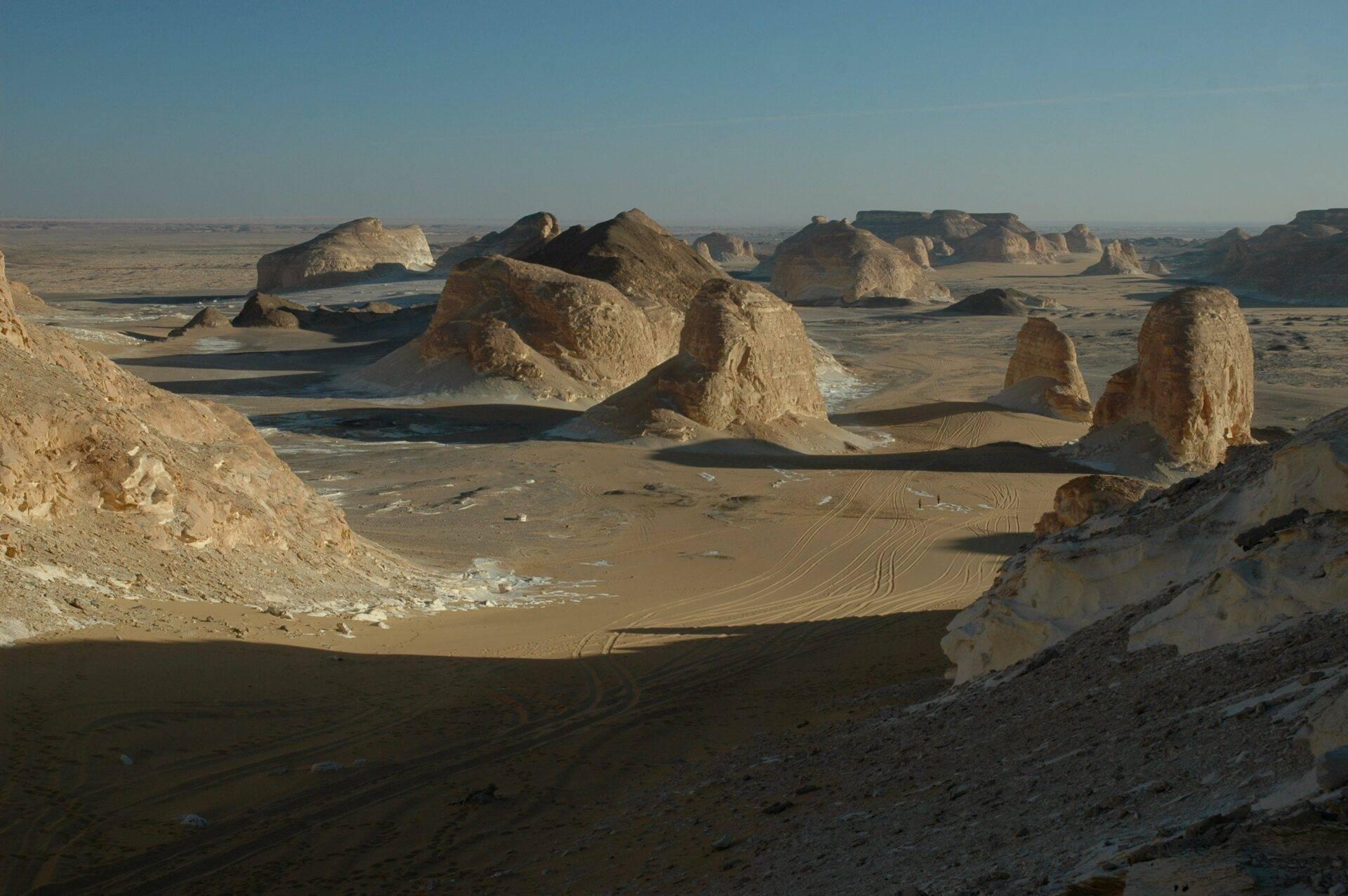 Spectacular limestone rock formations in an arid desert with vehicle tracks on the sandy floor