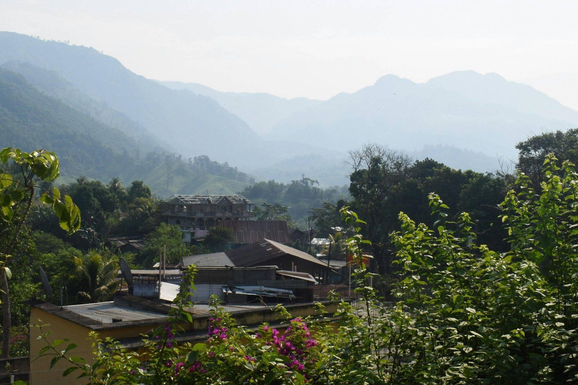 Vue sur une vallée montagneuse avec des bâtiments traditionnels entourés de végétation tropicale luxuriante