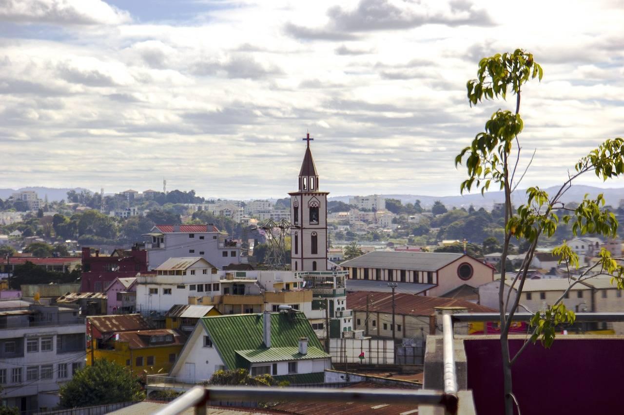 Panoramic view of a city with a white-steepled church rising above colourful rooftops against a mountainous backdrop