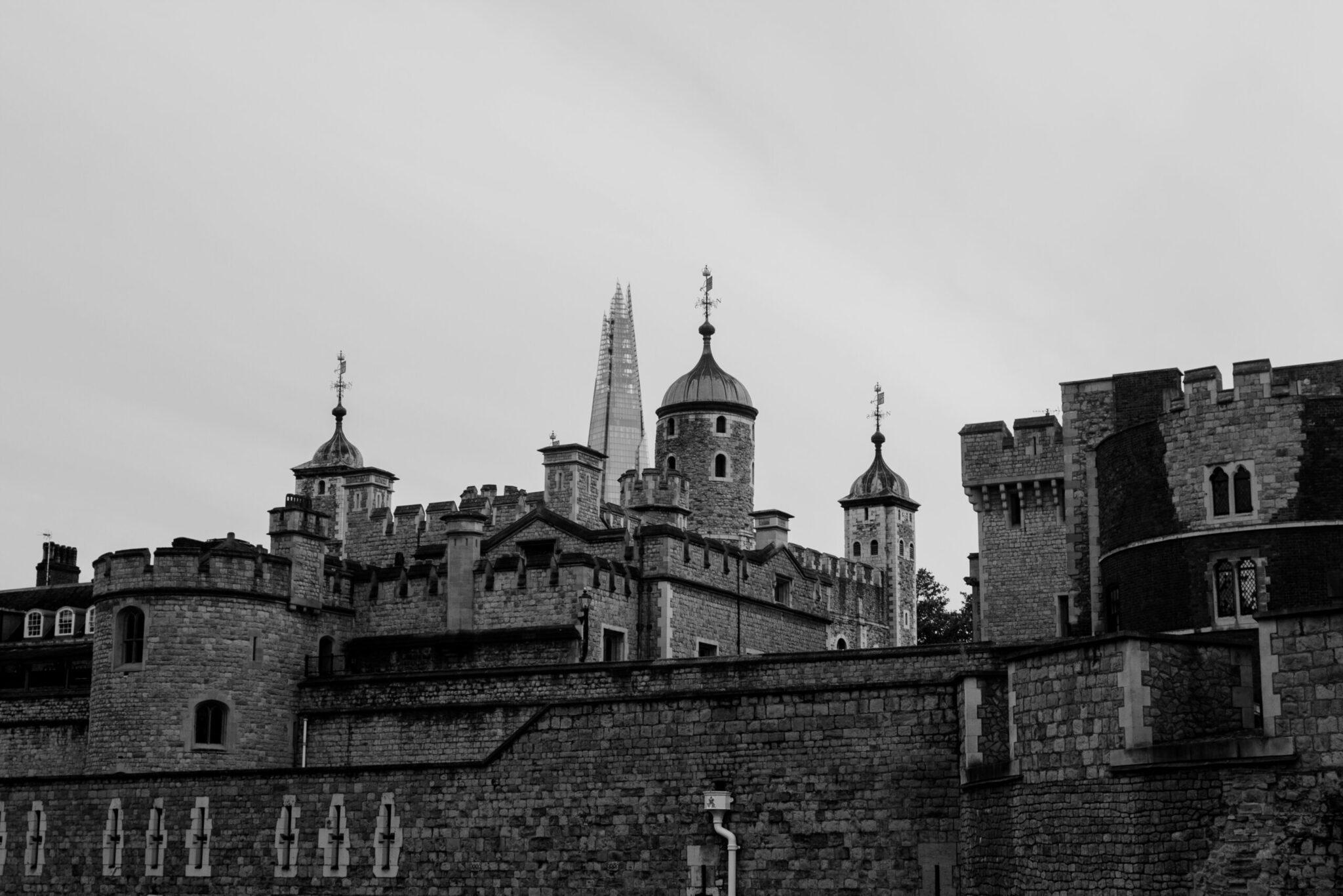 Forteresse médiévale en pierre avec tours crénelées et dômes, photographiée en noir et blanc sous un ciel nuageux