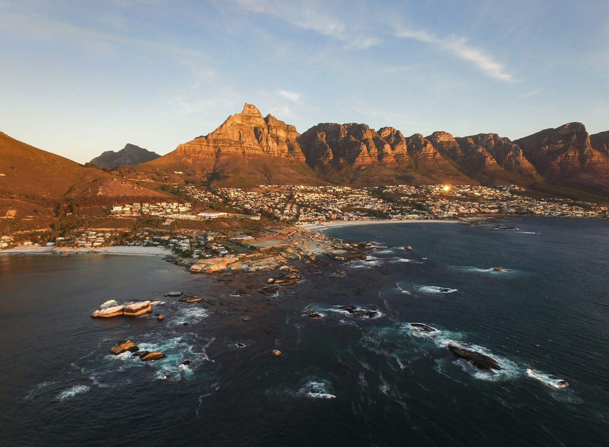 Aerial view of a coastal bay with steep mountains, a shoreline town and turquoise waters with emerging rocks