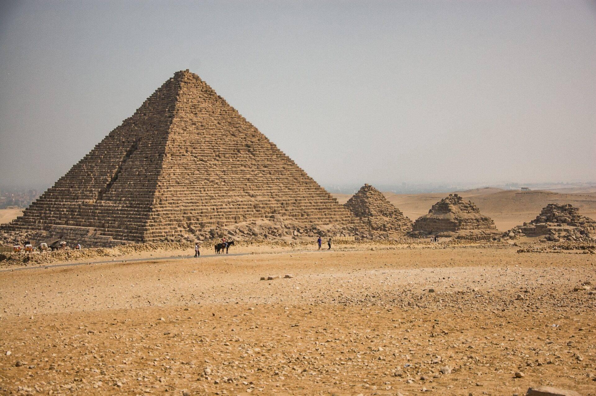 A vast stone pyramid in the Egyptian desert, with visitors and surrounding ruins under a clear sky