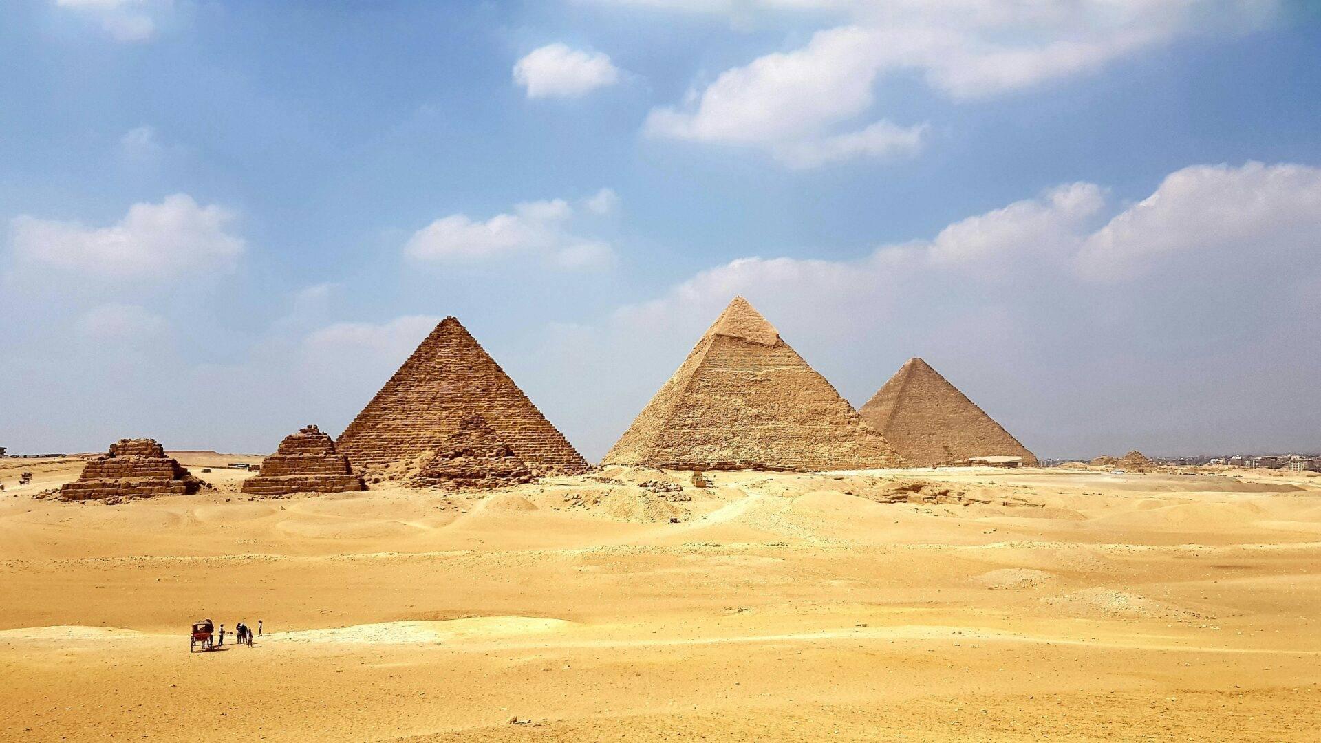 Three stone pyramids rising from an arid desert landscape under a clear blue sky, with visitors in the foreground