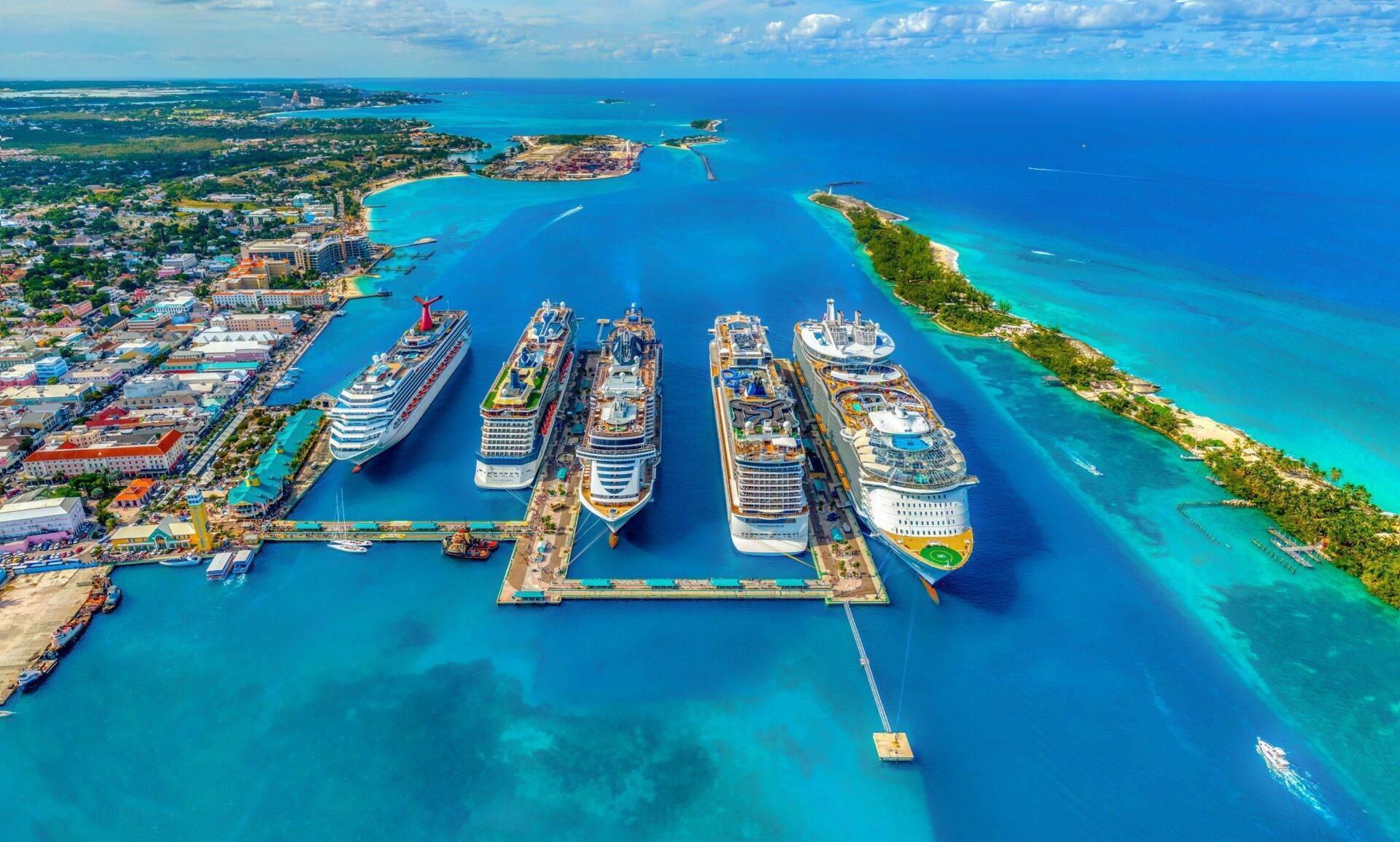 Vue aérienne d’un port de croisière tropical avec six navires amarrés dans une baie turquoise entourée d’îles verdoyantes