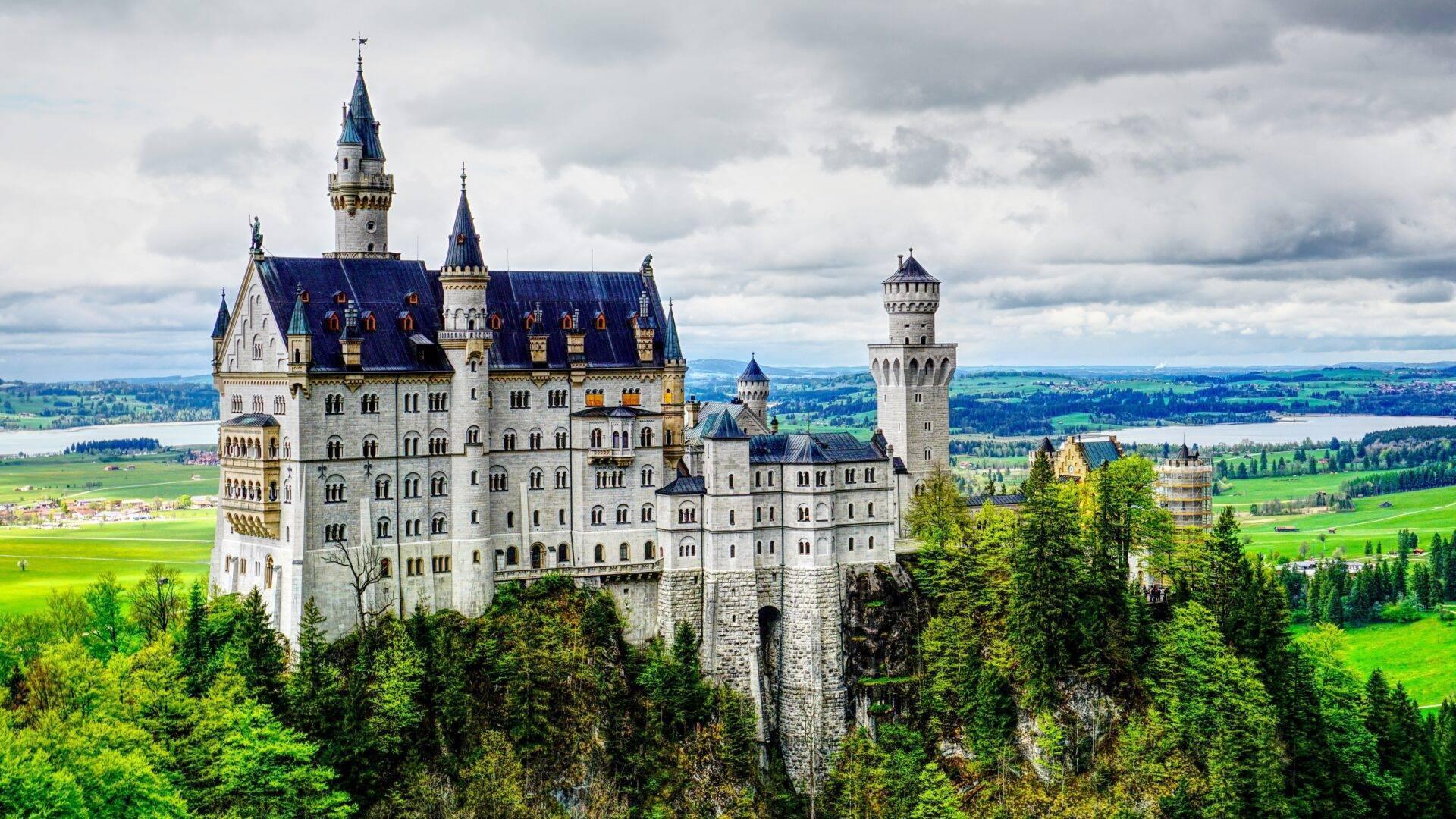 A majestic white castle with pointed turrets perched on a rocky cliff, surrounded by conifer forests and green valleys