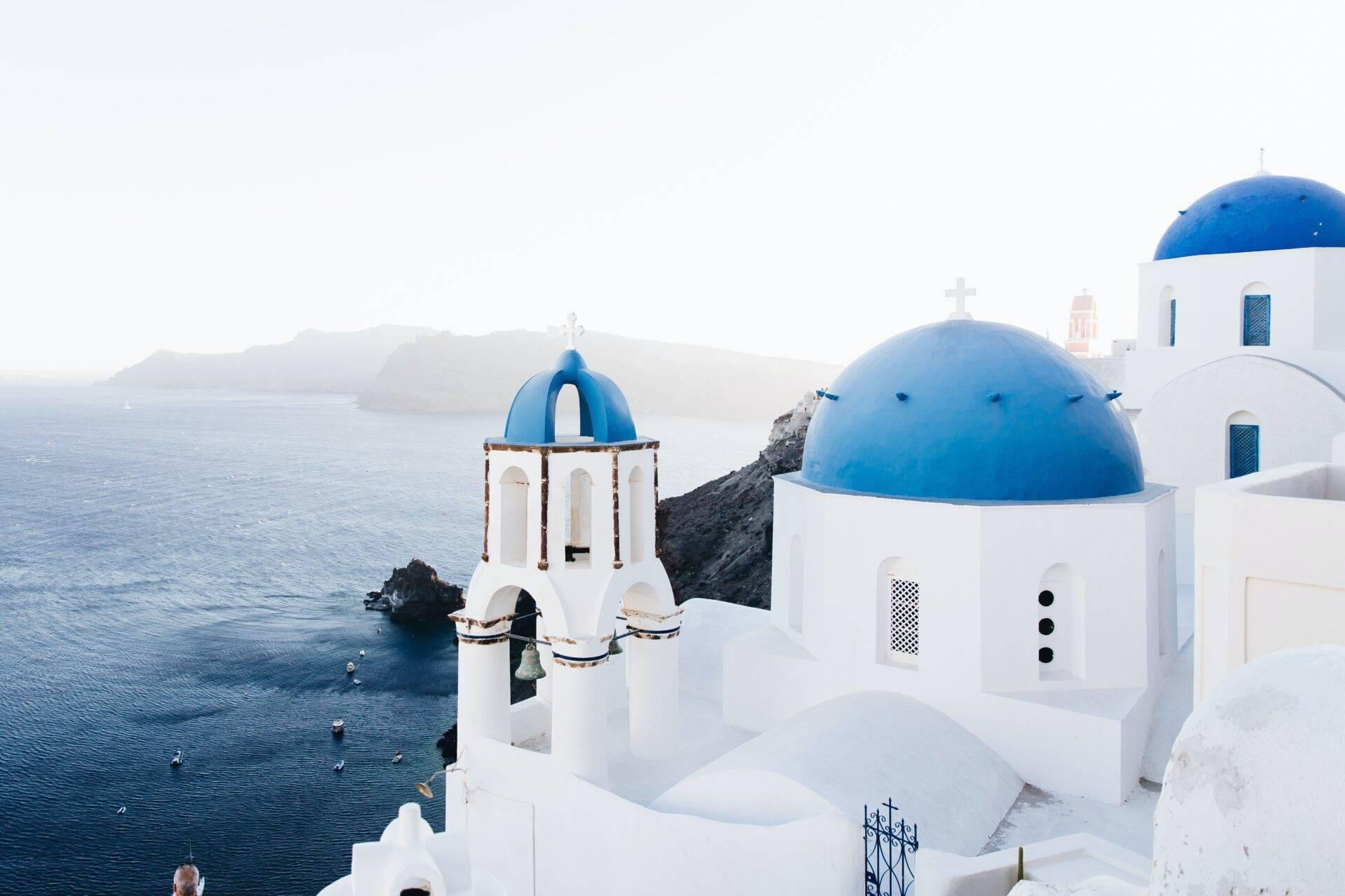White churches with blue domes overlooking the Mediterranean Sea, typical Cycladic architecture of the Greek islands