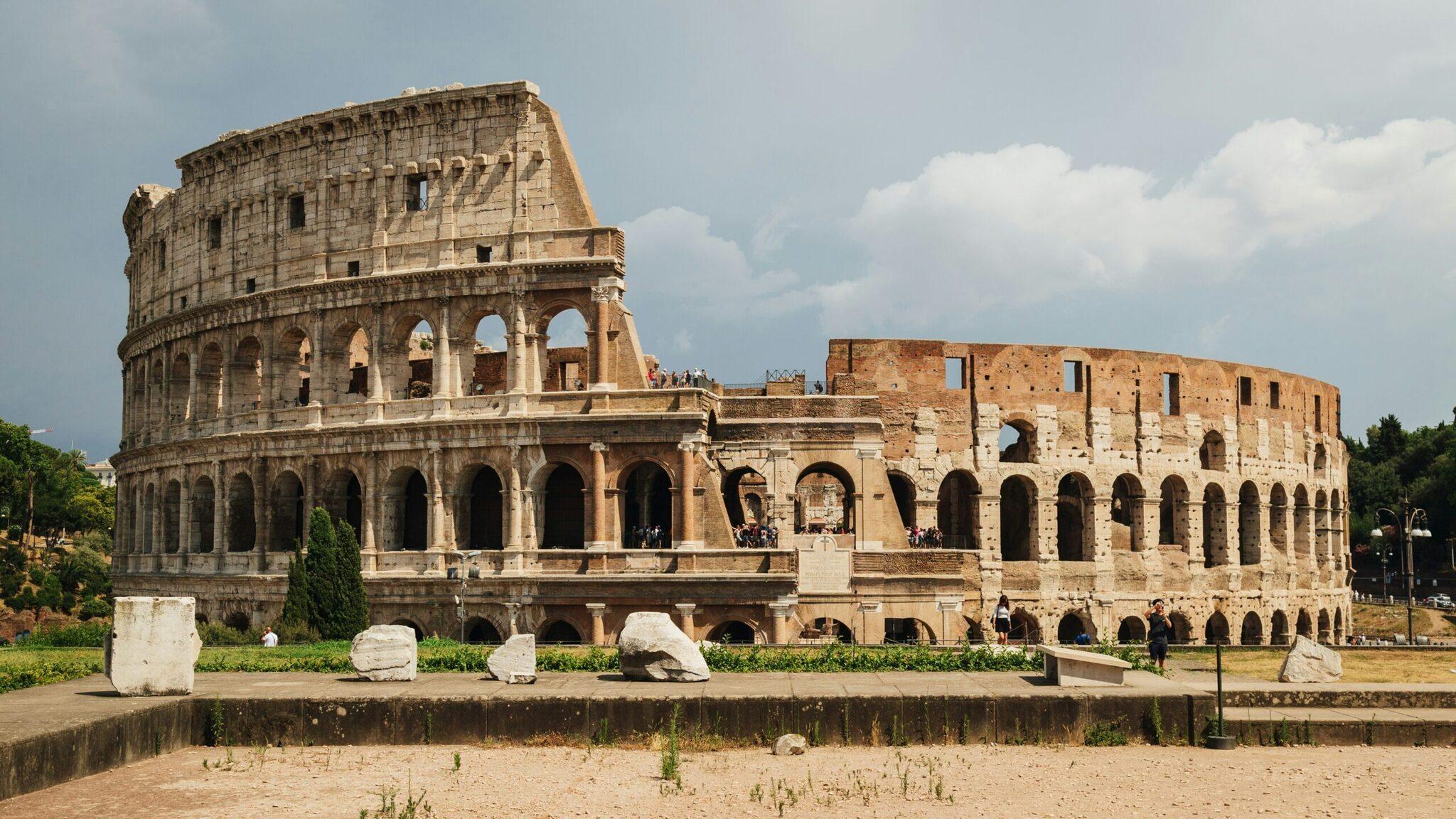 The majestic ruins of the ancient Colosseum in Rome, with its tiered arches and partially preserved seating under a clear blue sky