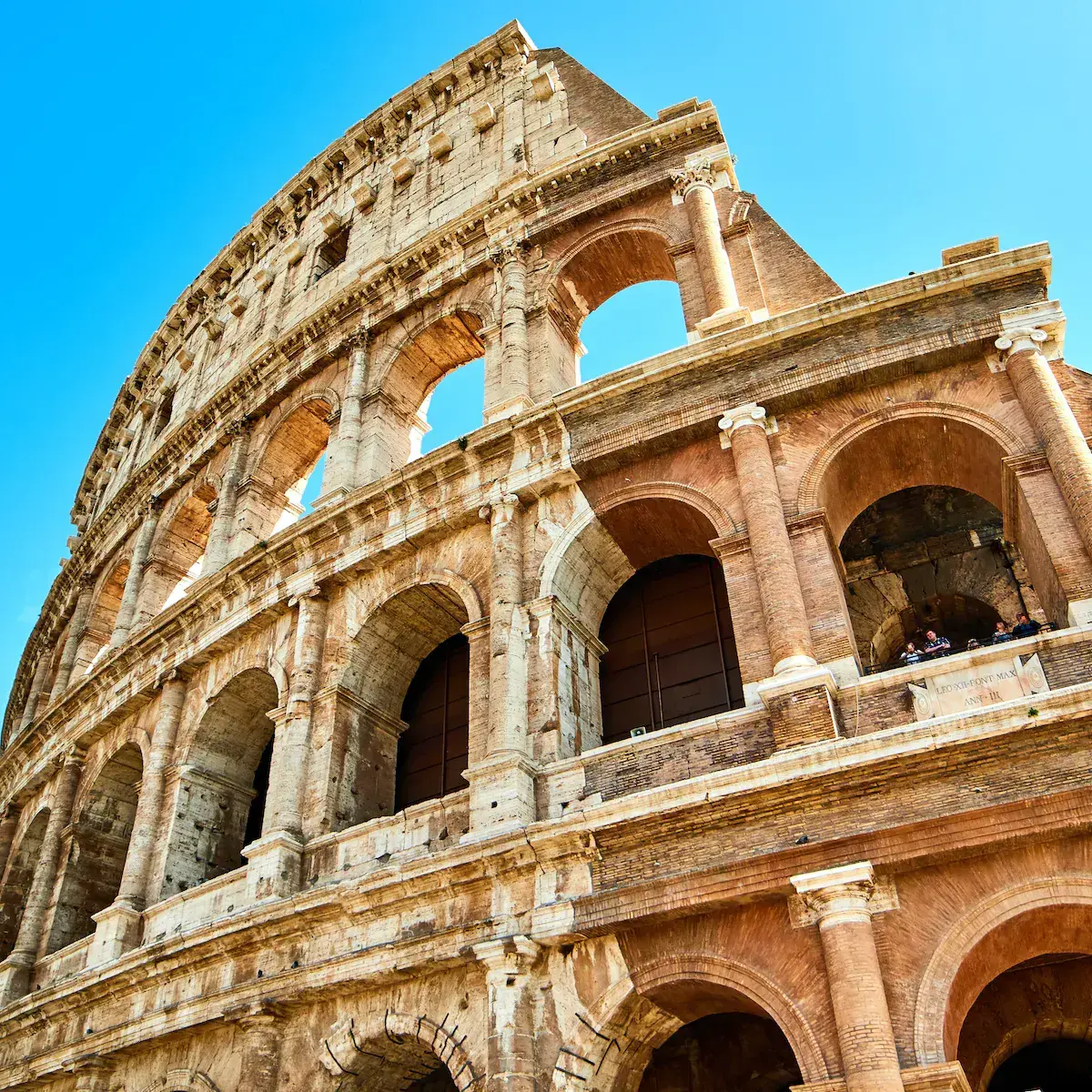 Les vestiges d’un amphithéâtre antique en pierre avec arcades superposées sous un ciel bleu dégagé