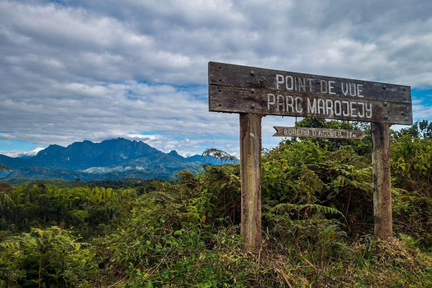 Wooden signpost pointing to a viewpoint in Marojejy Park, with a panoramic view over the forested Malagasy mountains behind