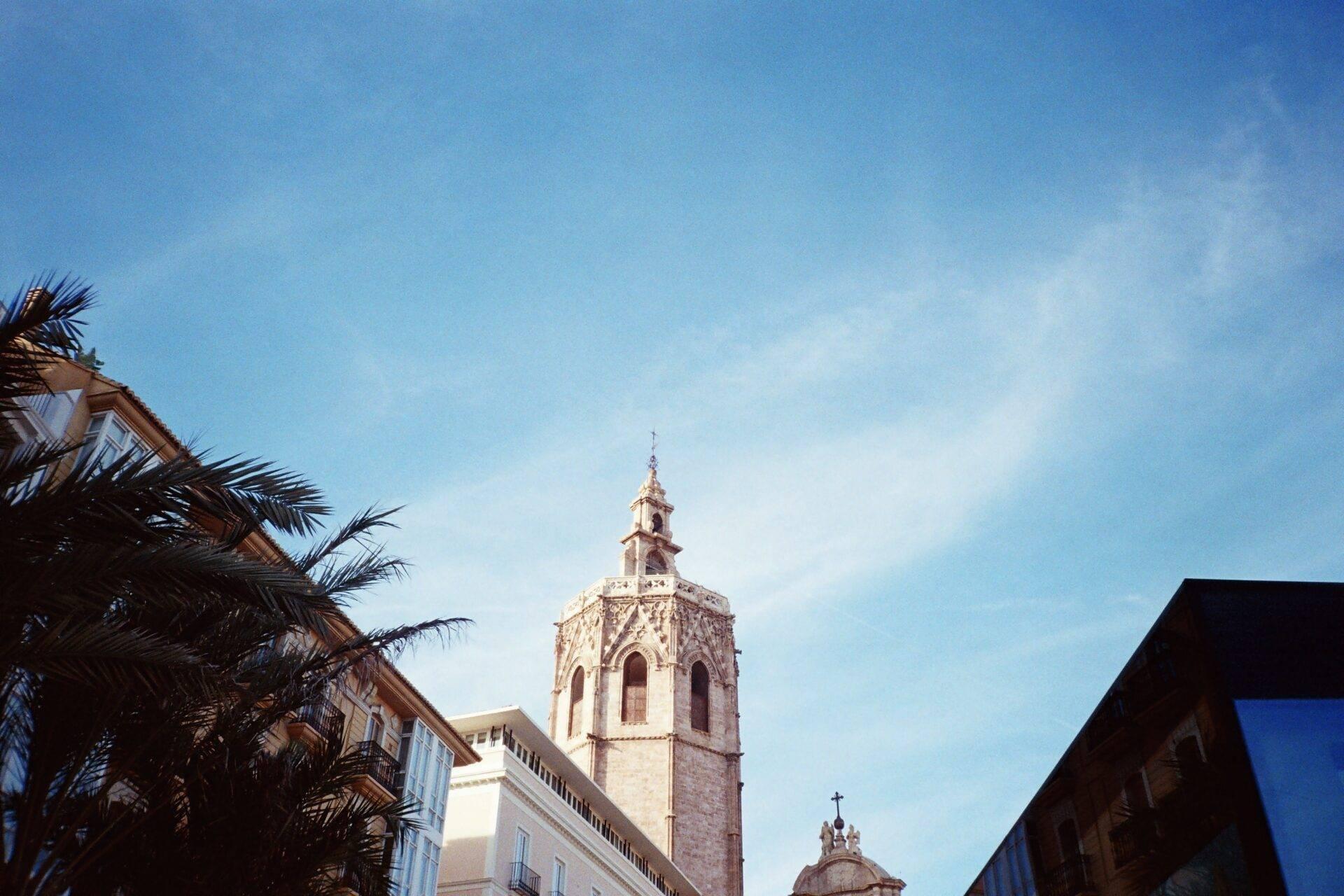 Clocher baroque d’une église espagnole encadré par des palmiers et bâtiments coloniaux sous ciel bleu