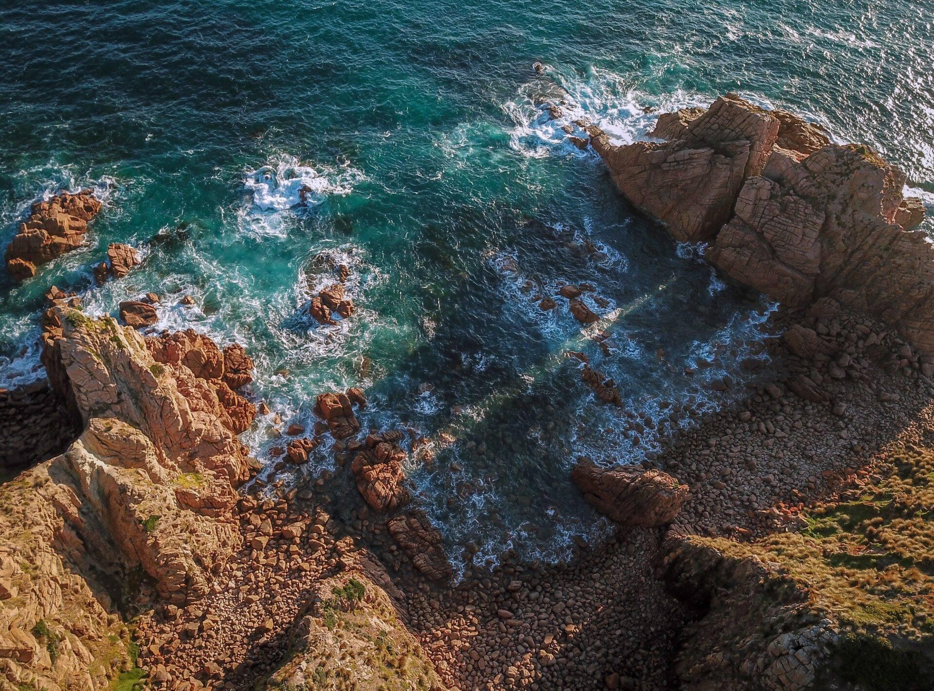 Vue aérienne d’une côte rocheuse avec falaises rouges, vagues turquoise et formations géologiques spectaculaires