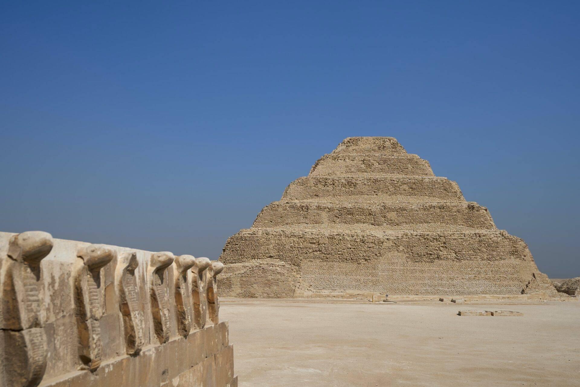 A limestone step pyramid in the Egyptian desert with architectural details in the foreground
