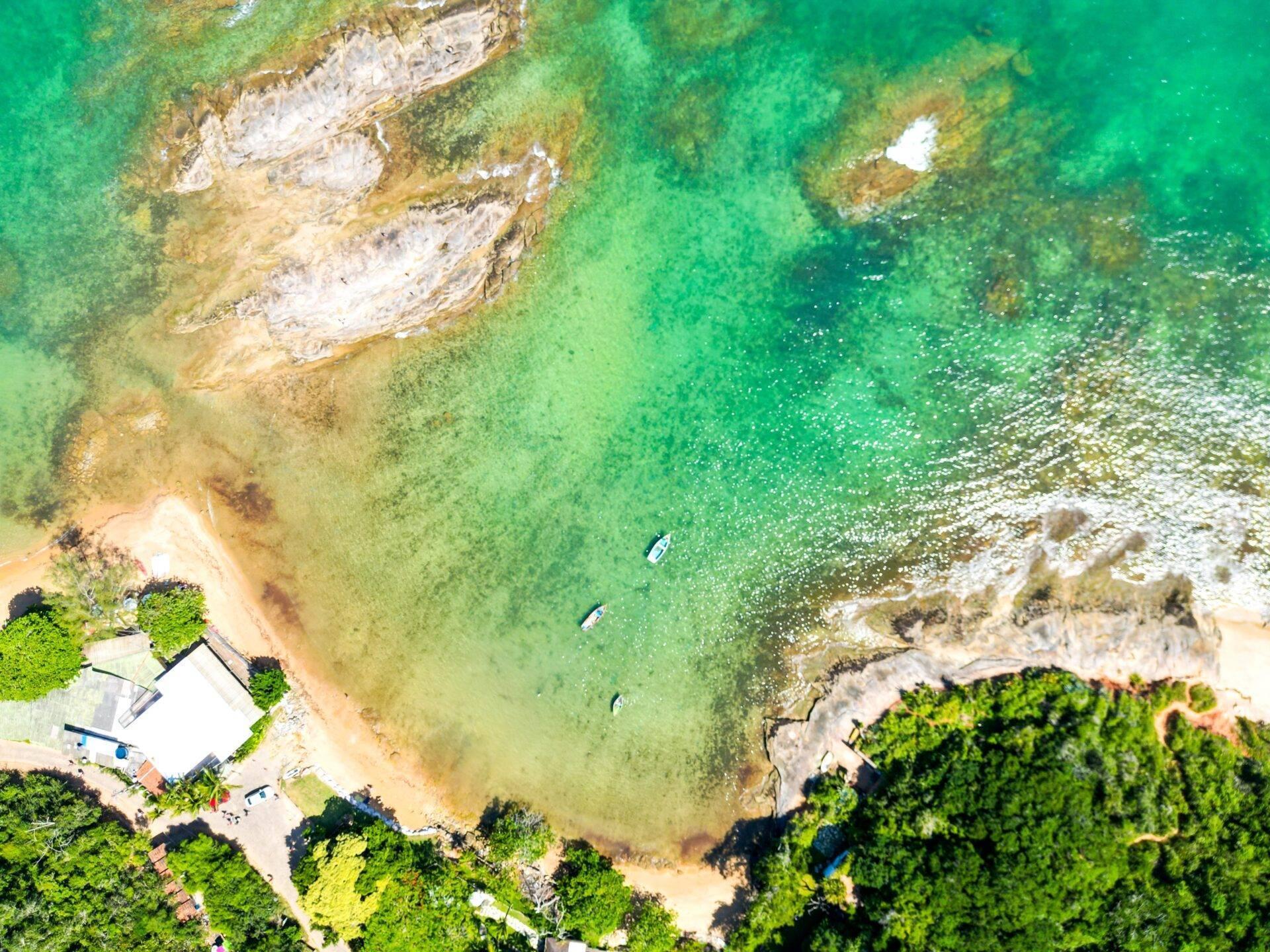 Aerial view of a small coastal cove with a sandy beach, crystal-clear turquoise water and white rocky formations