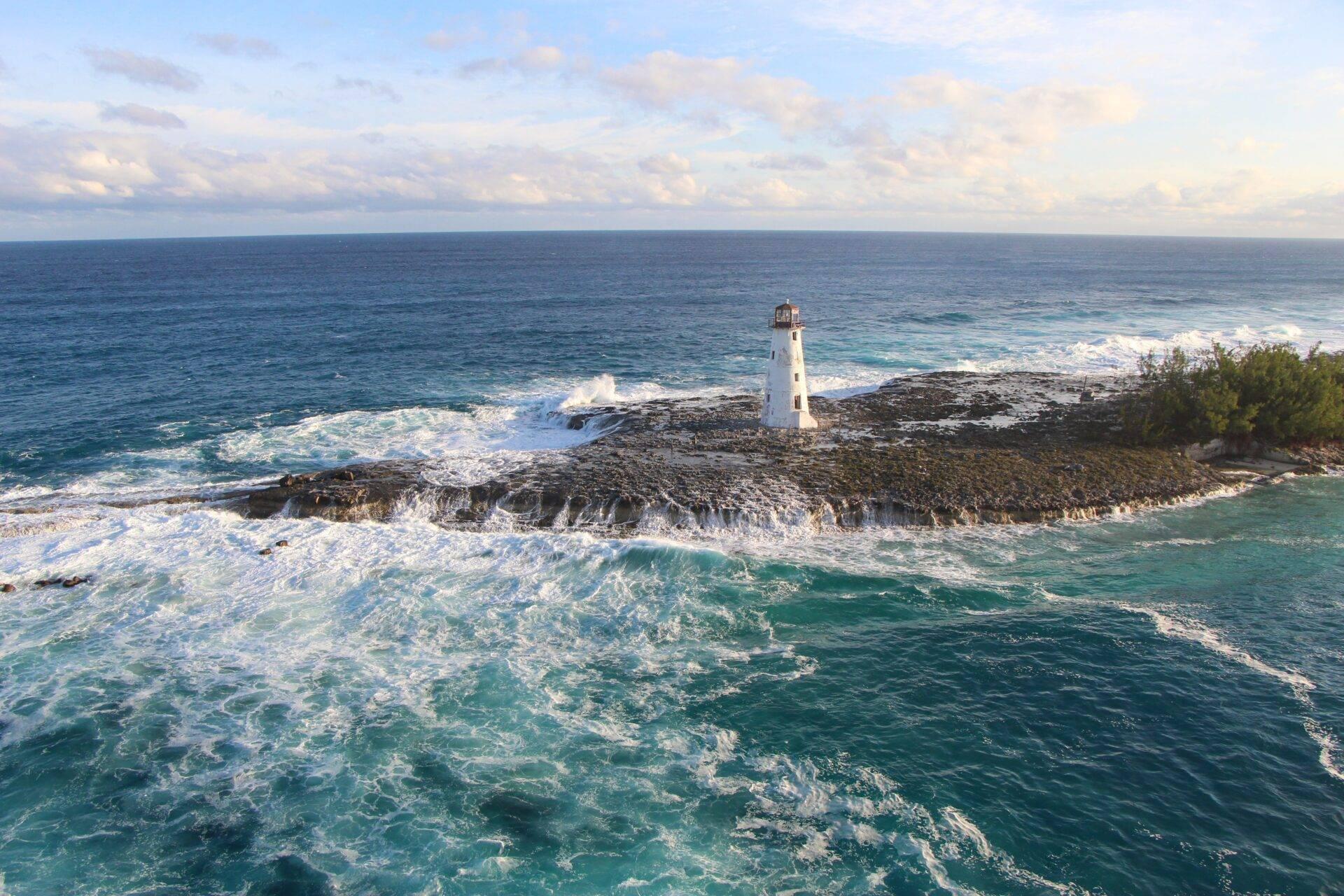 Phare blanc sur une pointe rocheuse battue par les vagues de l’océan turquoise aux Bahamas