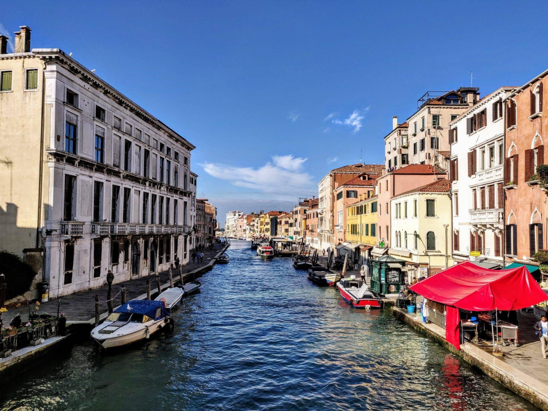 A Venetian canal lined with colourful palaces, with gondolas and boats moored in fine weather