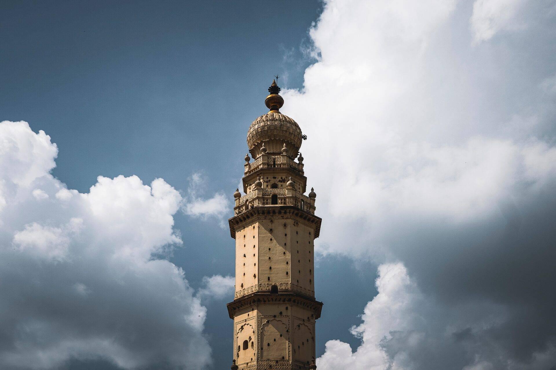 Ancient ochre stone minaret with ornamental balconies under a partly cloudy blue sky