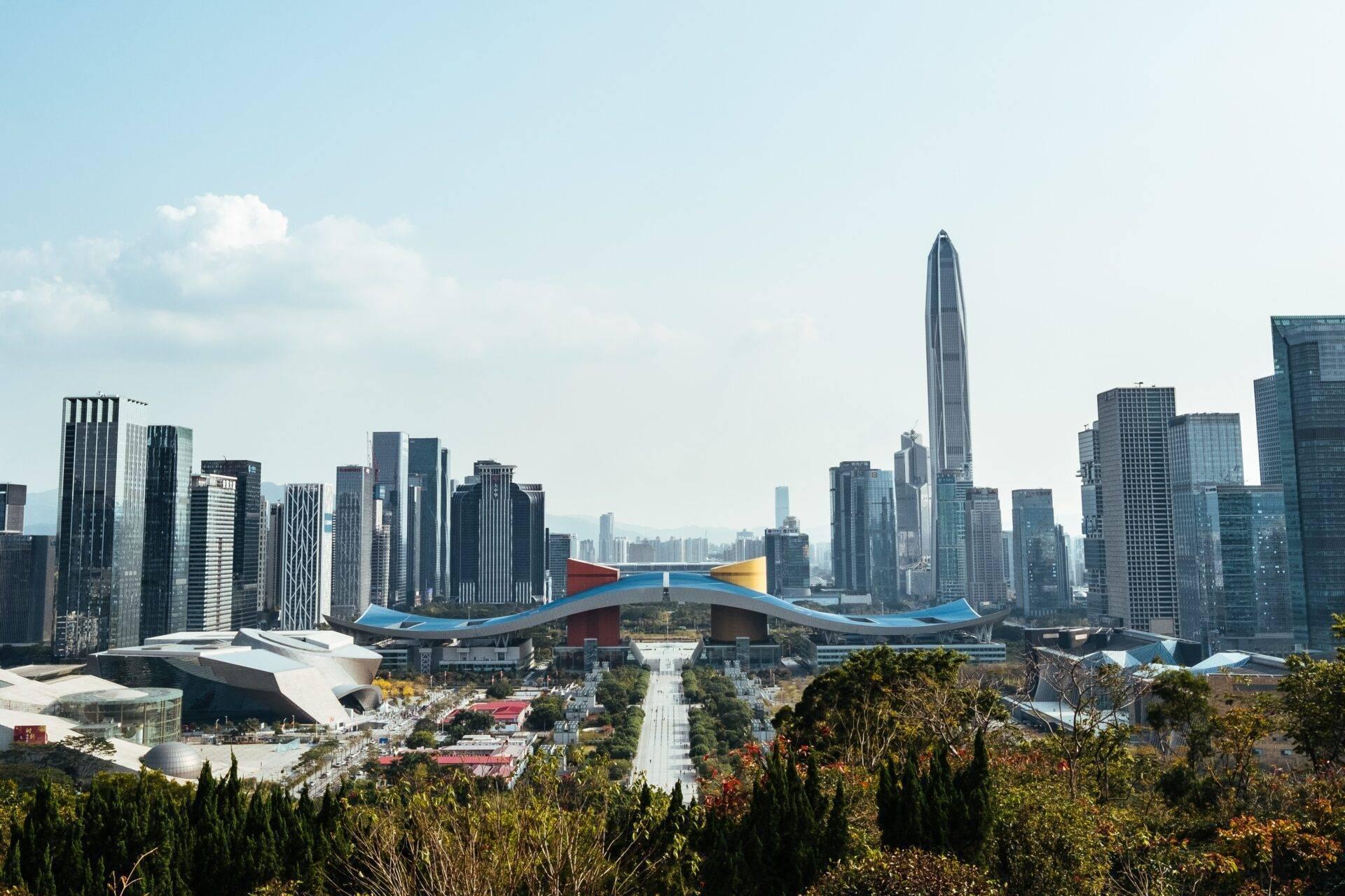 Vue panoramique d’une ville moderne avec gratte-ciel, bâtiment architectural bleu et rouge au premier plan, parc verdoyant et ciel dégagé