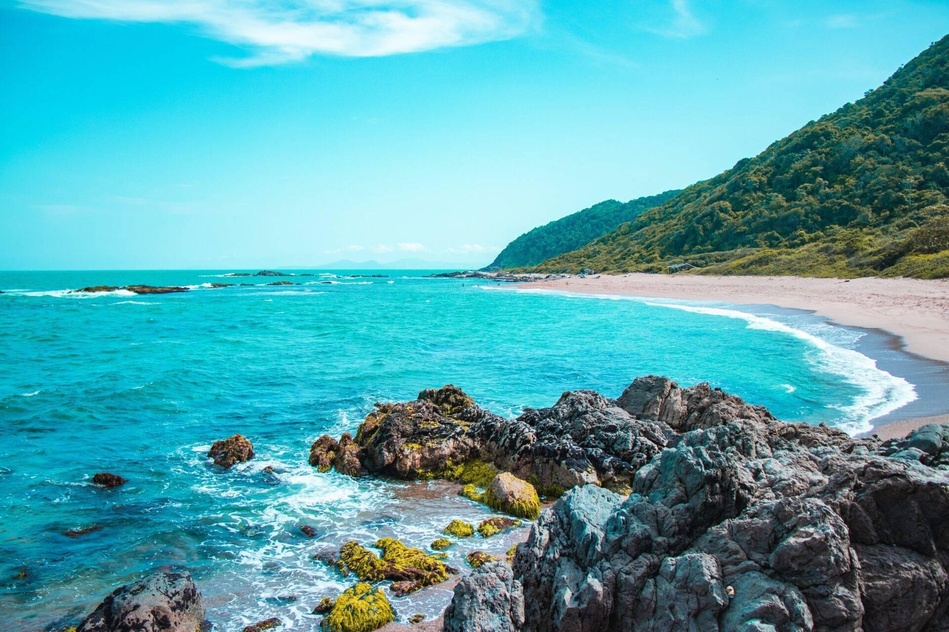 Baie tropicale avec plage de sable blanc, rochers couverts de mousse, forêt luxuriante et mer turquoise cristalline