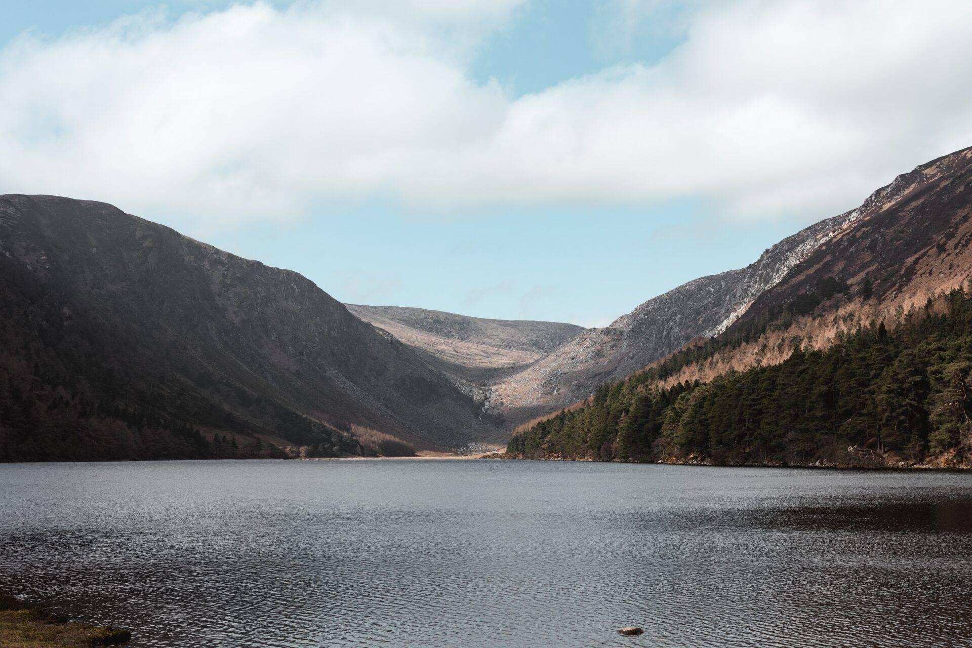 A mountain lake framed by wooded hills and rocky slopes under a cloudy sky