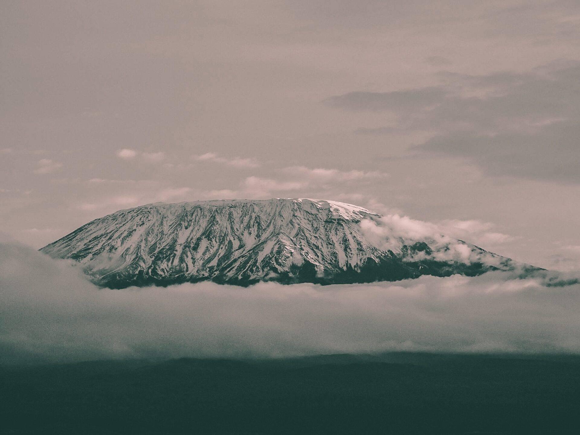 A snow-capped summit with striated slopes emerging from the clouds, majestic high-altitude mountain landscape