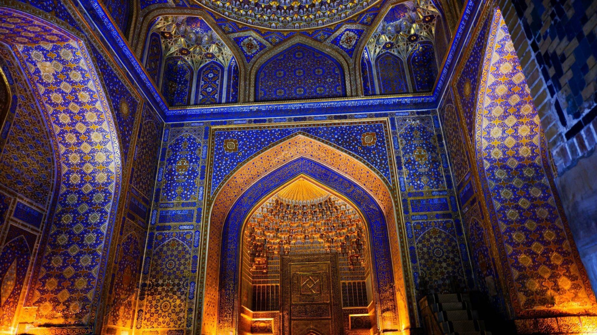 Richly decorated mosque interior with cobalt-blue walls, golden ornaments and a monumental illuminated doorway